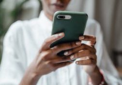 A woman in a white blouse using her smartphone indoors, showing a thoughtful and calm mood.